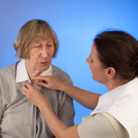 Caretaker dressing an elderly woman